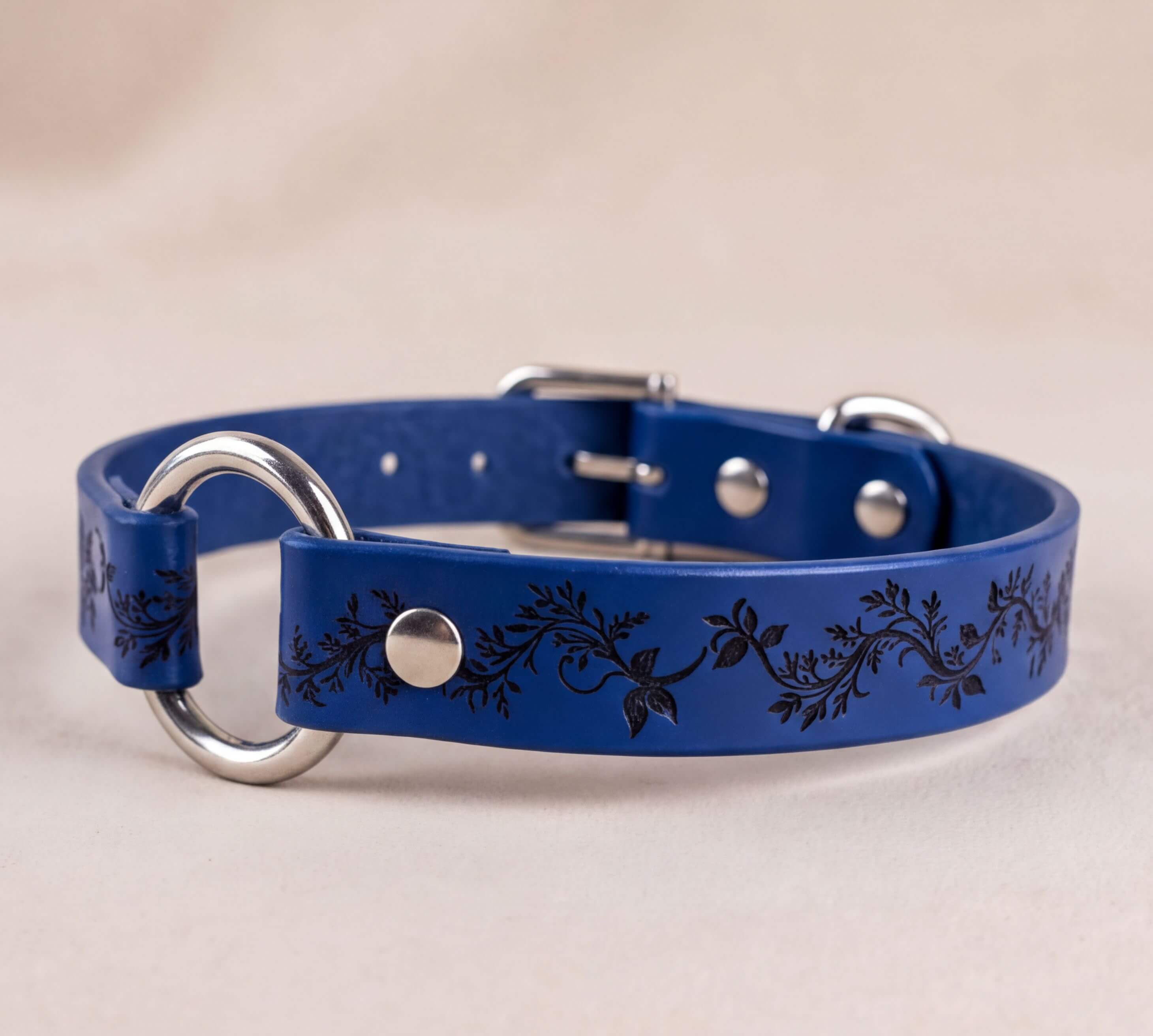 A blue leather dog collar with a floral pattern and metal rings.
