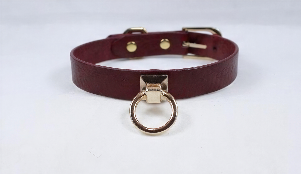 A burgundy leather choker collar with a gold-colored metal ring and buckle.