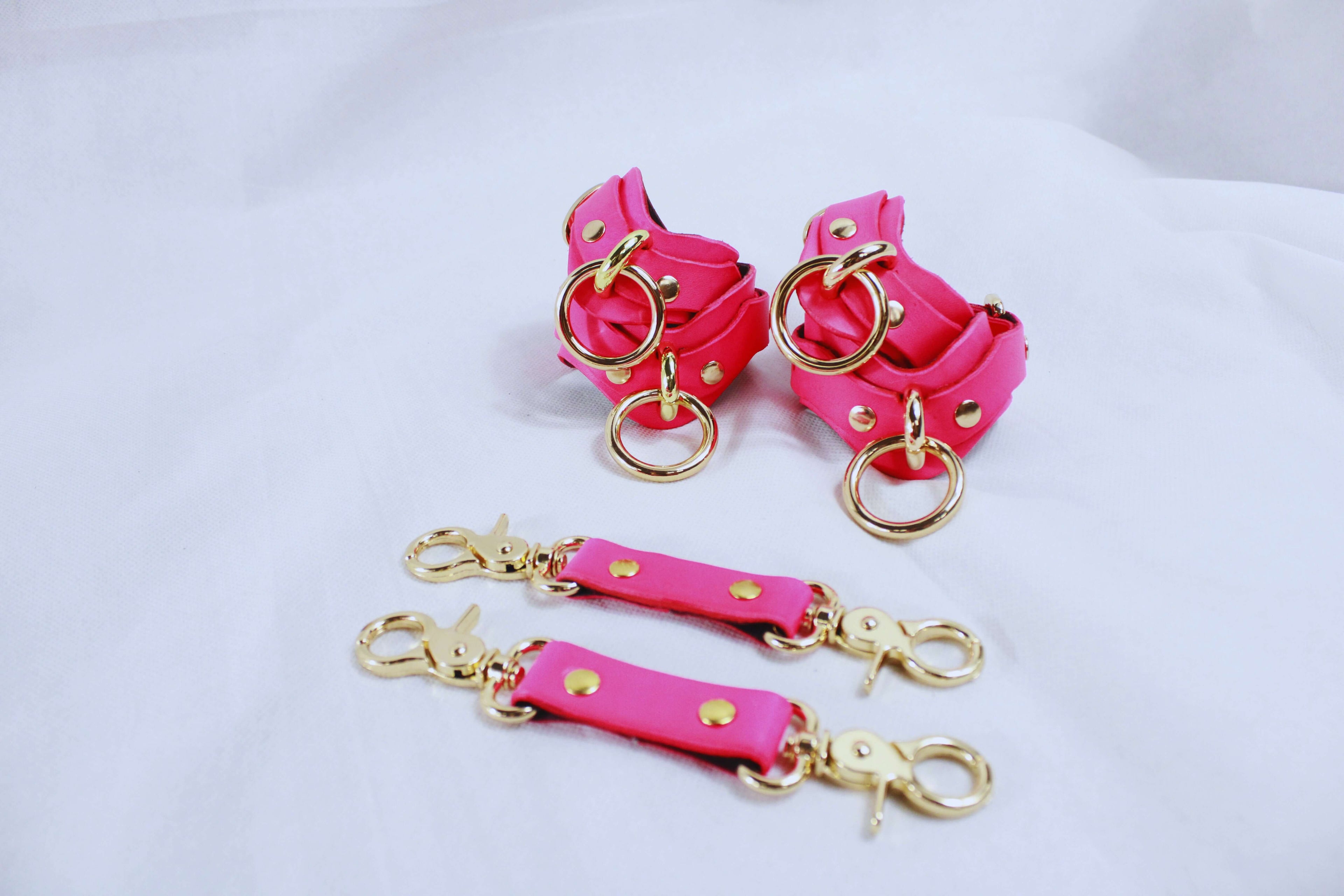 Pink bondage cuffs and connectors with gold accents, ideal for submissive play and BDSM experiences.