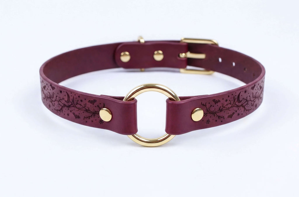 A burgundy leather choker collar with a gold-colored metal ring and buckle.