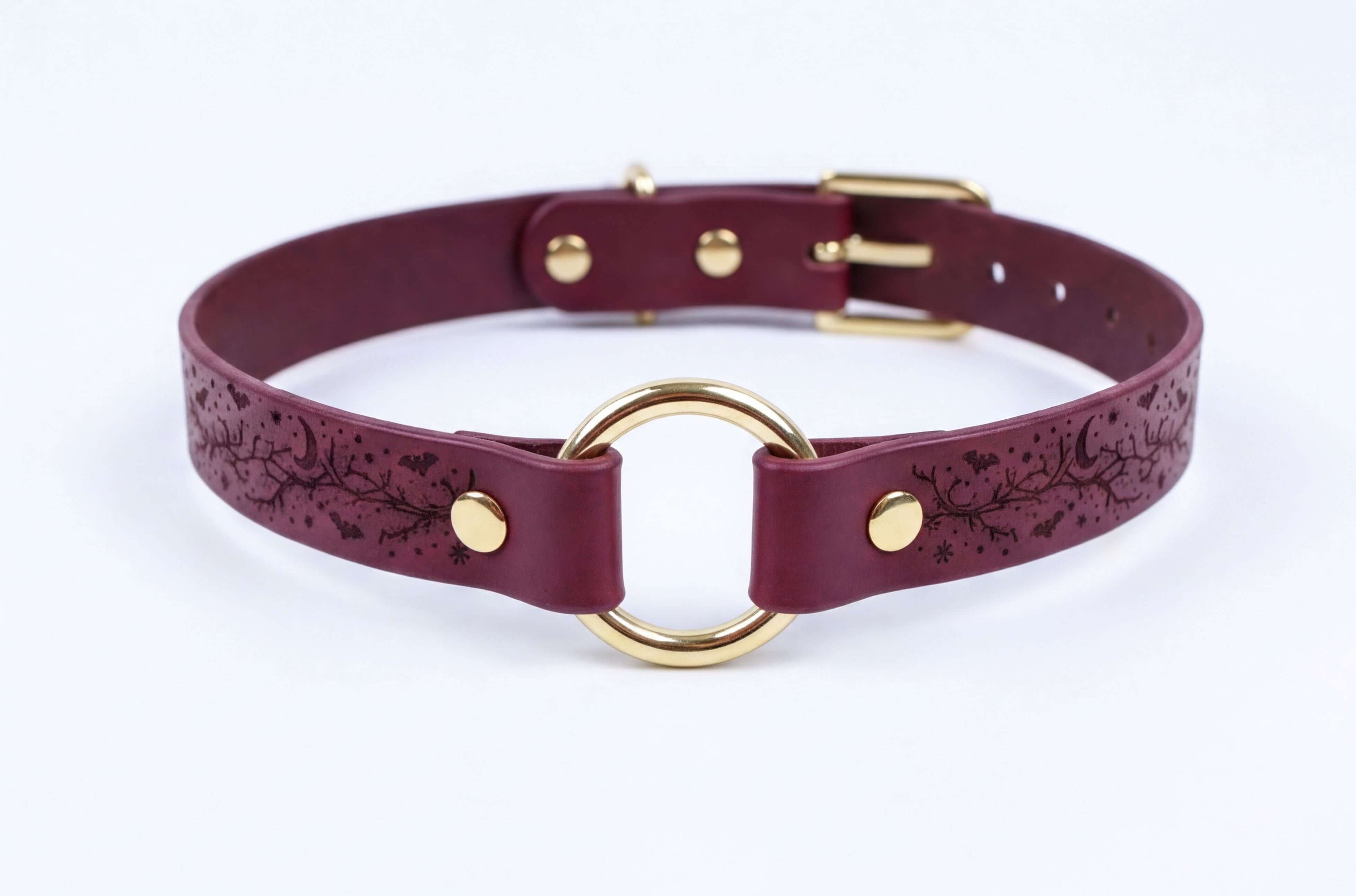A burgundy leather choker collar with a gold-colored metal ring and buckle.