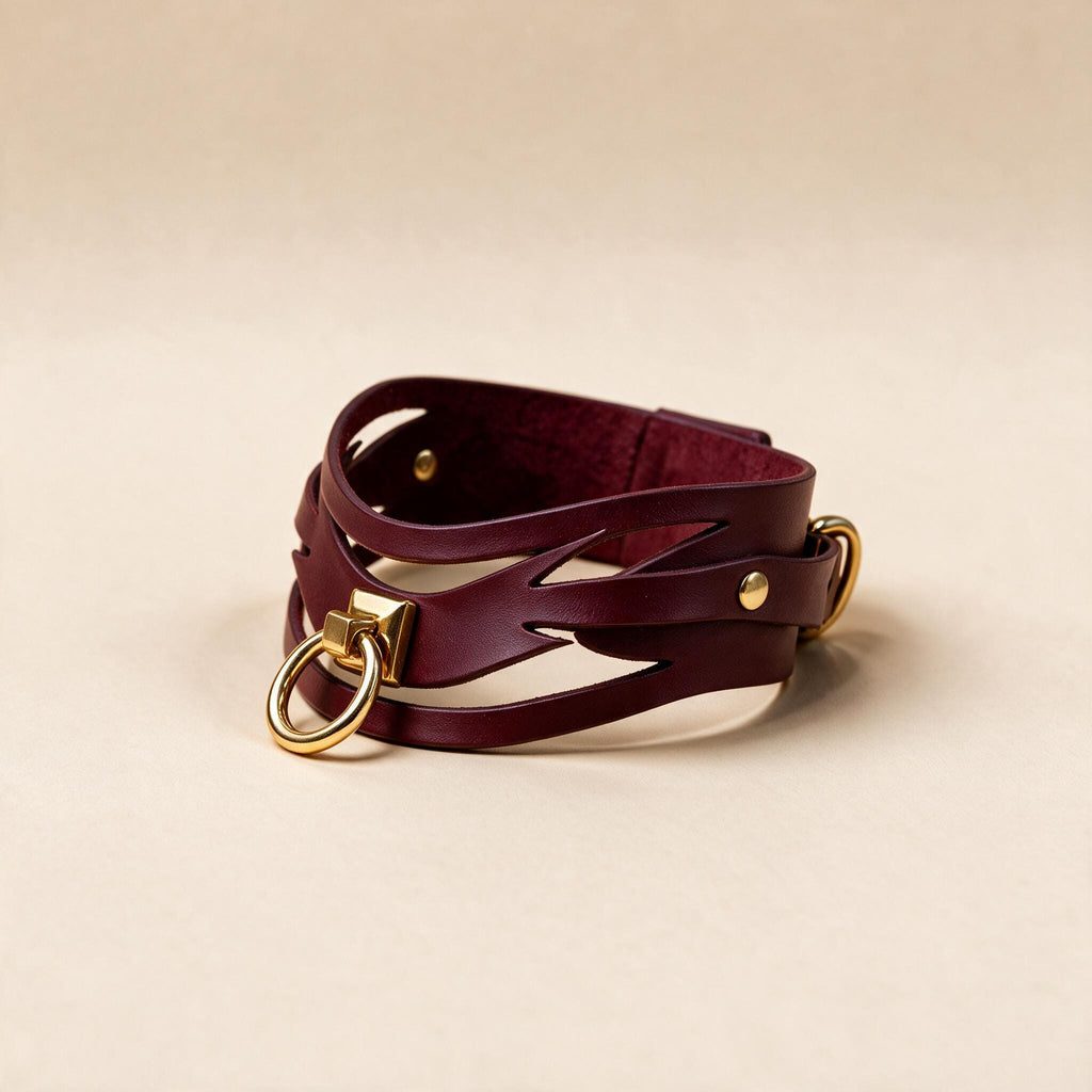 A burgundy leather choker necklace with a gold-colored metal clasp and a gold-colored metal ring.