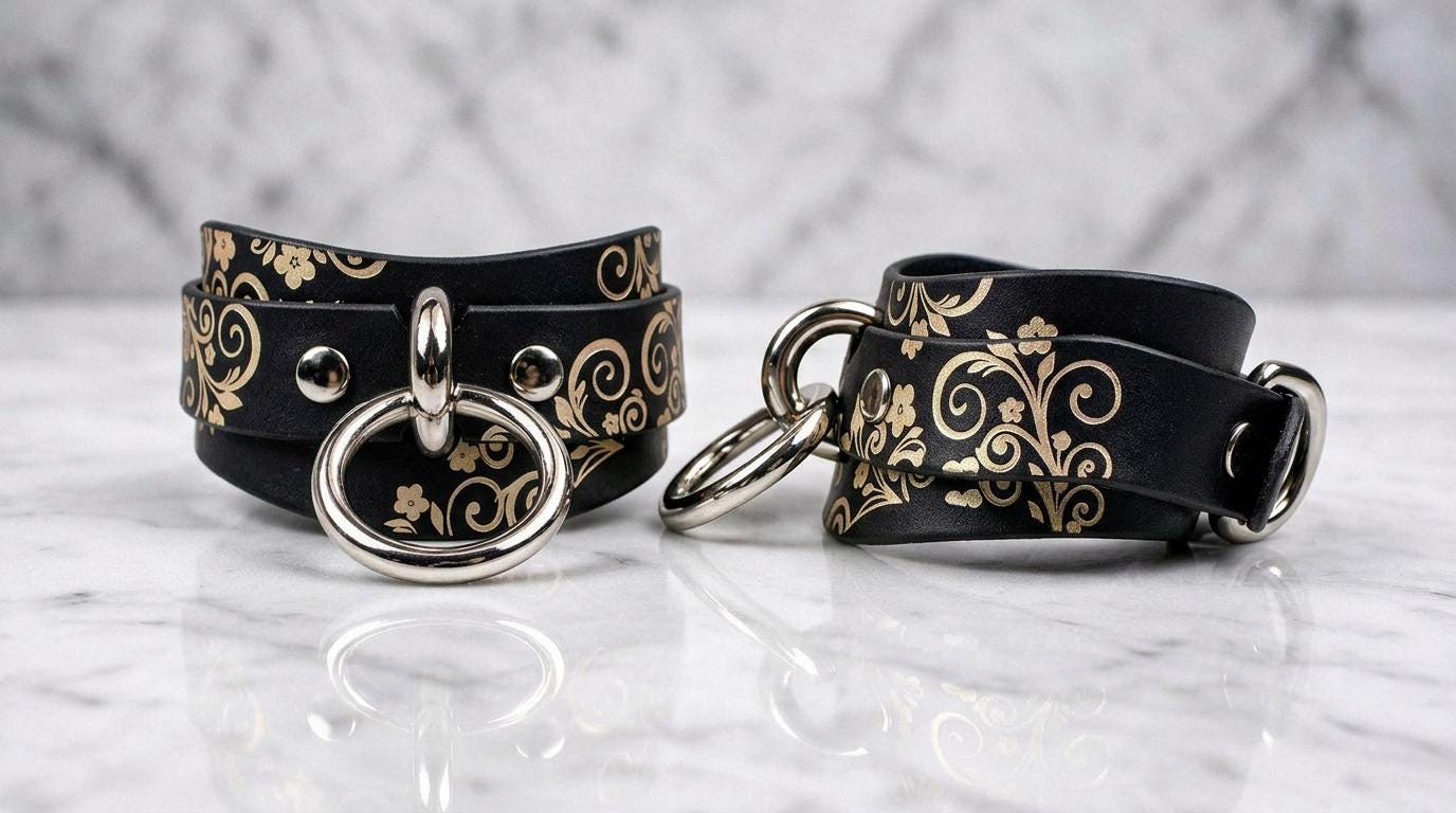 a pair of black leather straps with gold floral designs, placed on a marble surface.