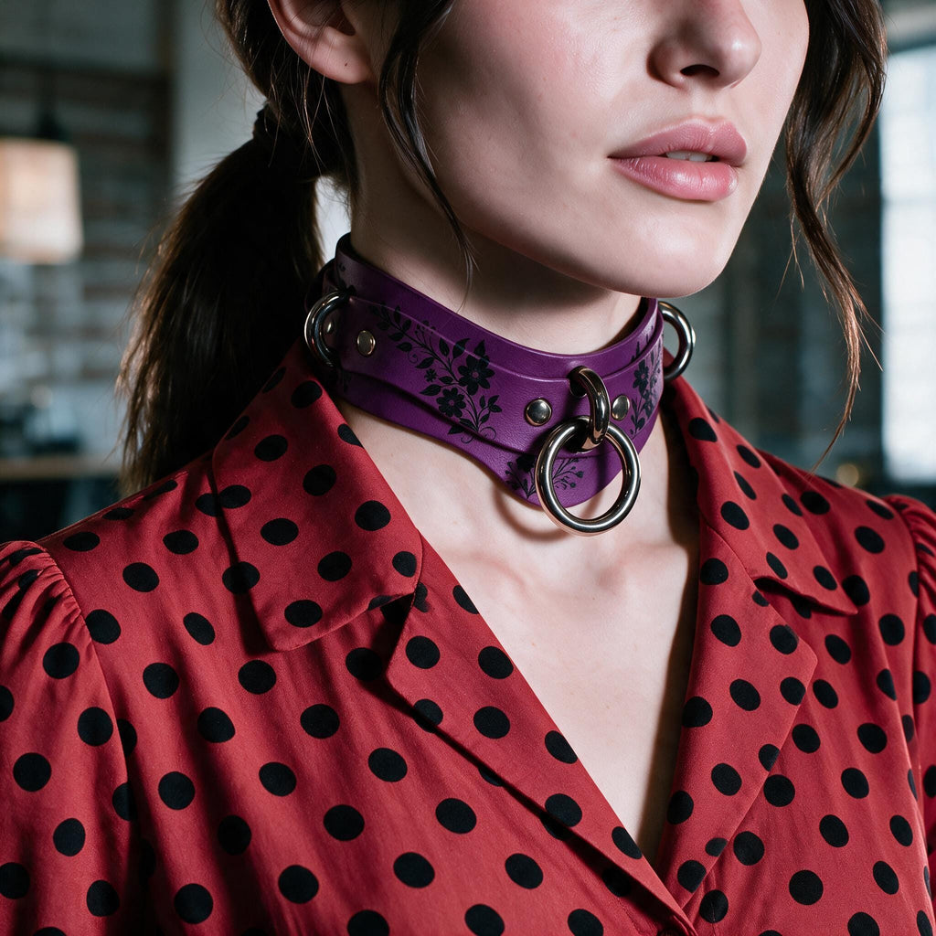 A close-up of a woman wearing a purple choker necklace with metal rings, paired with a red polka dot blouse.