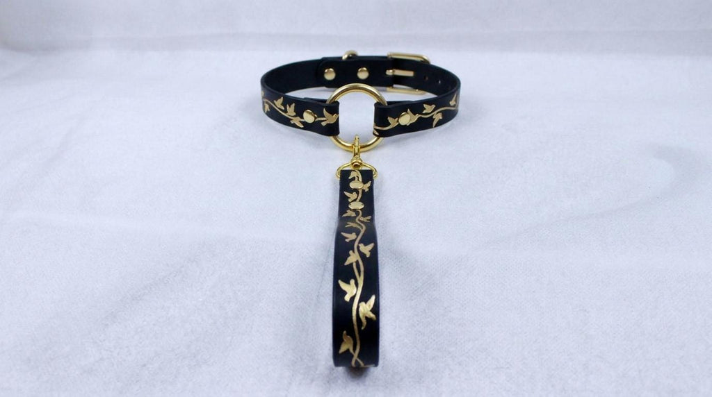A black collar with gold leaf designs and a gold-colored loop hanging from it.