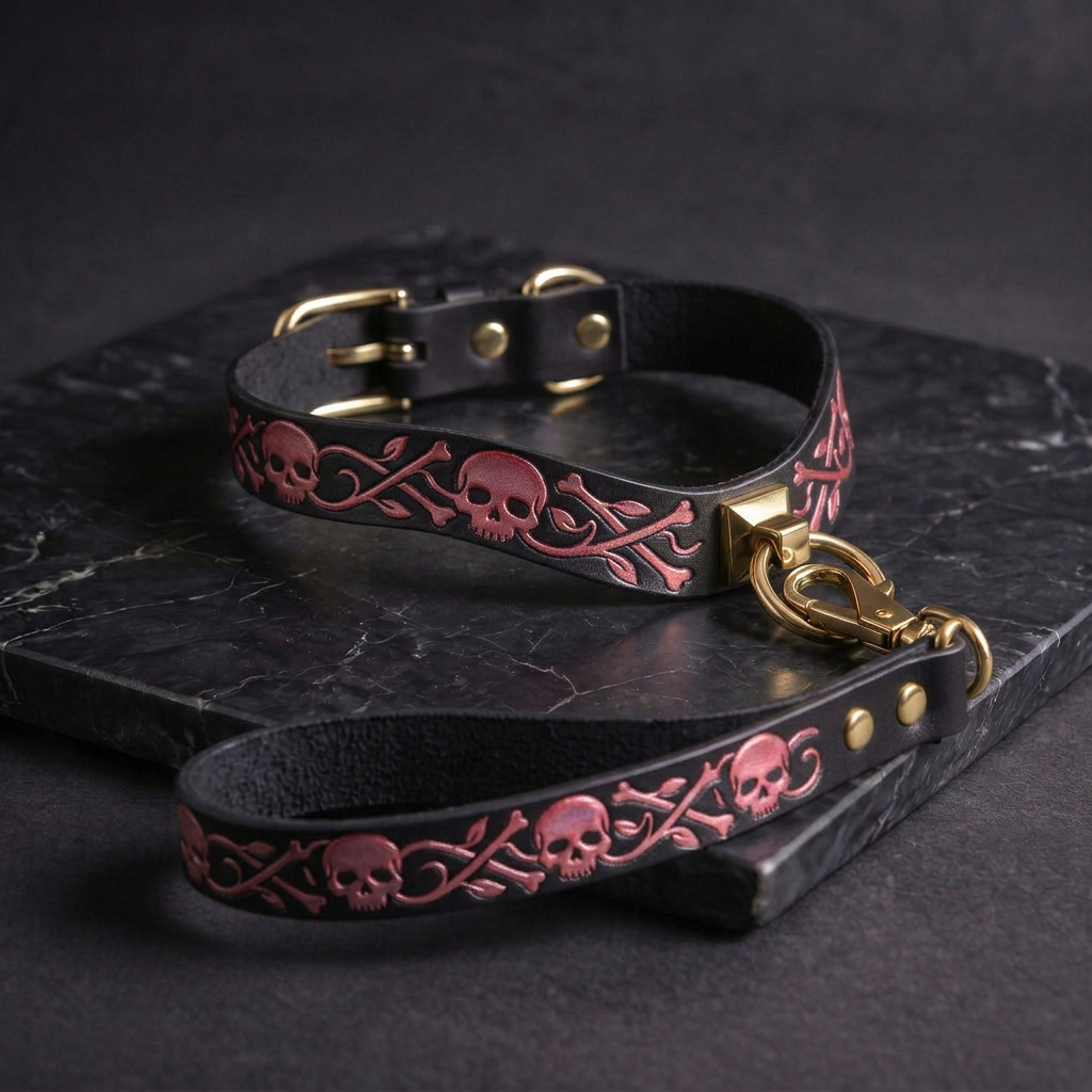 A black leather collar with a pink skull and bone design, and a matching black leash with a gold buckle, both resting on a dark surface.