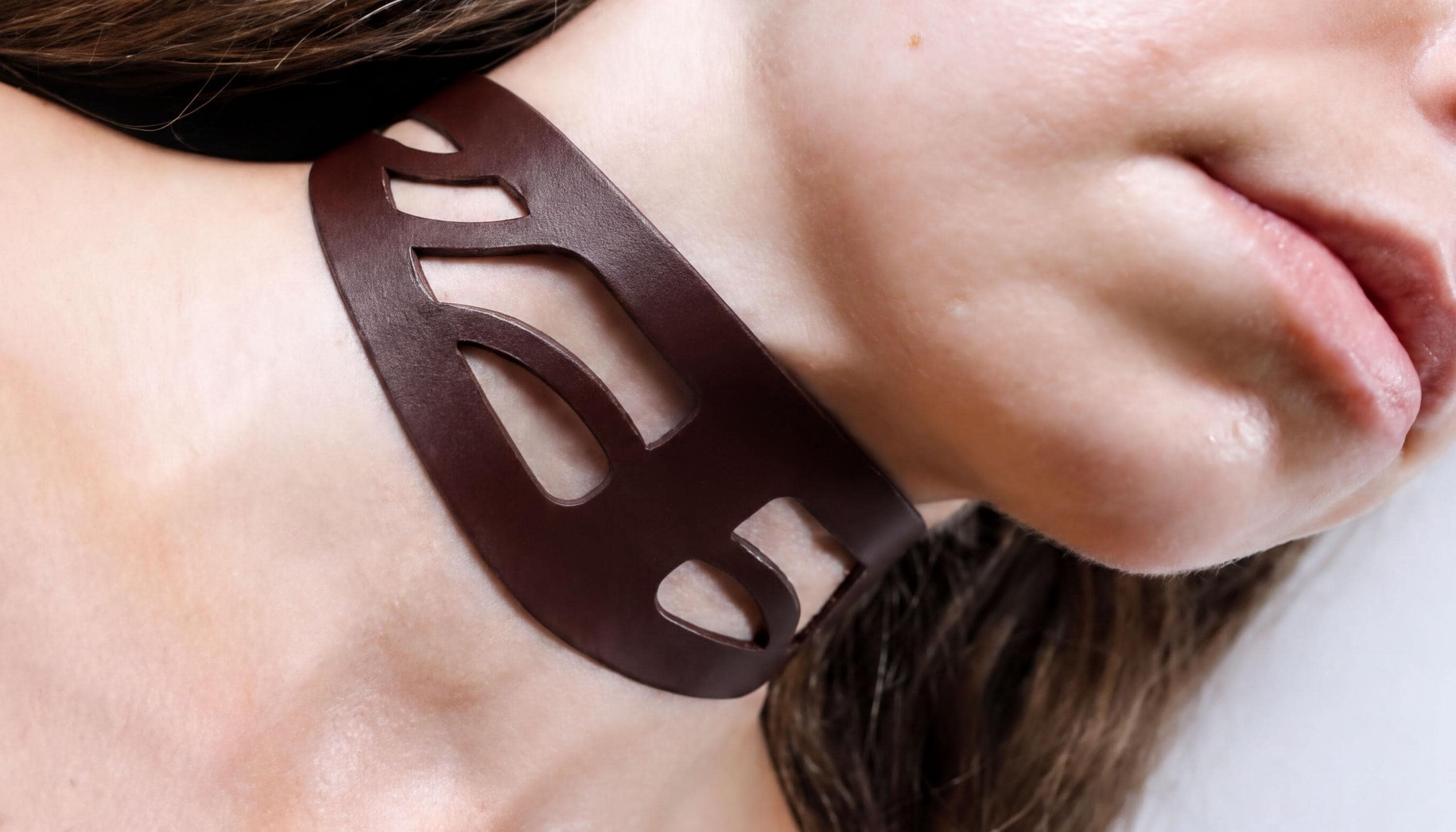 A close-up of a woman's neck and chin wearing a brown leather choker necklace.