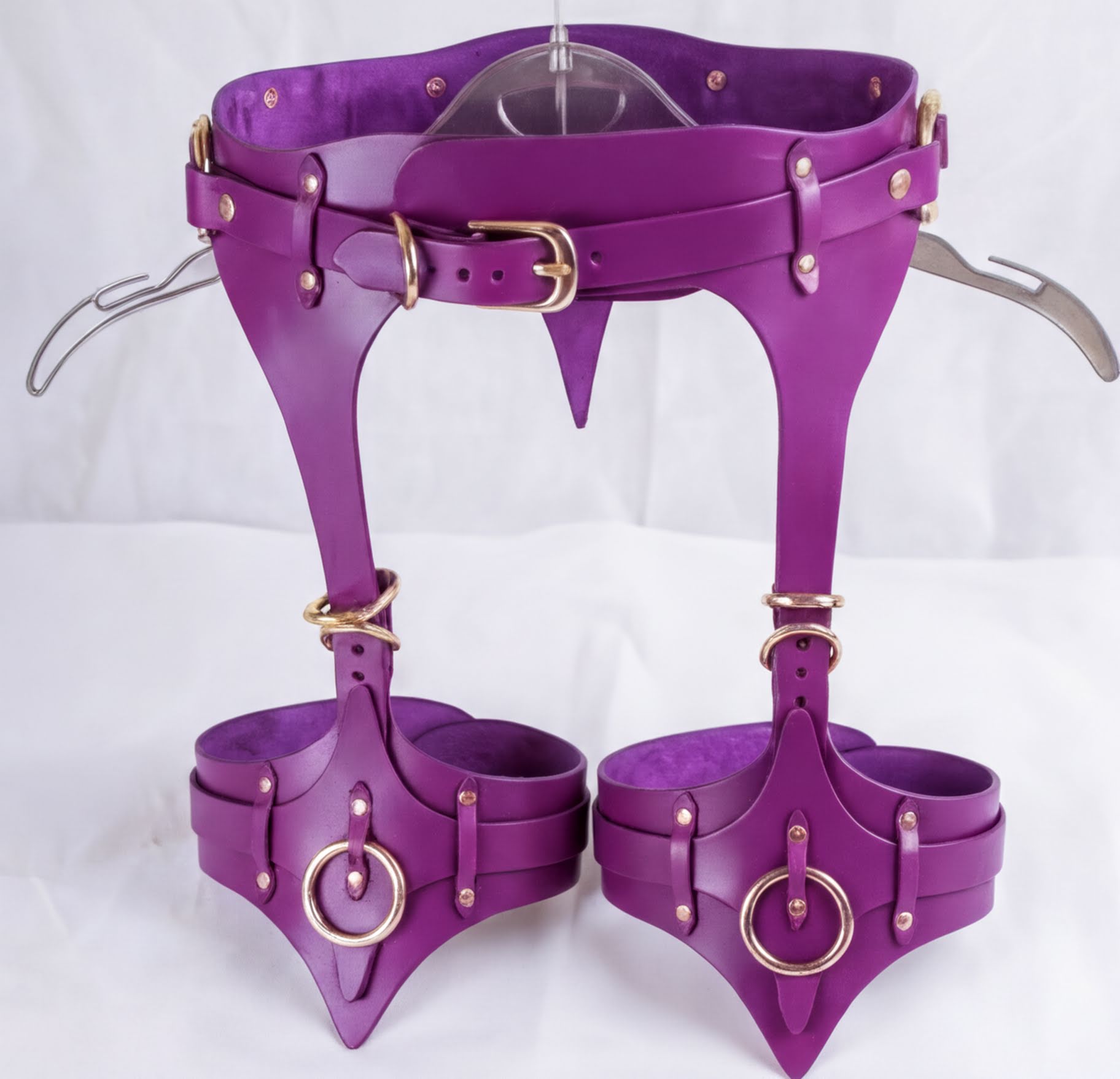 A pair of purple leather straps with gold hardware, including buckles and rings, attached to a belt.