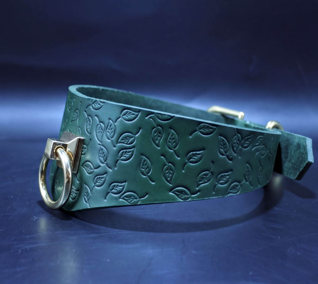 A green leather collar with a leaf pattern embossed on it, featuring a gold-colored metal ring and buckle.