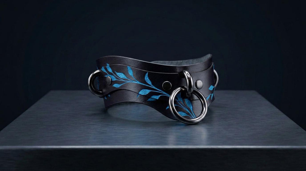 A black leather choker necklace with blue leaf designs and metal rings is displayed on a dark surface.
