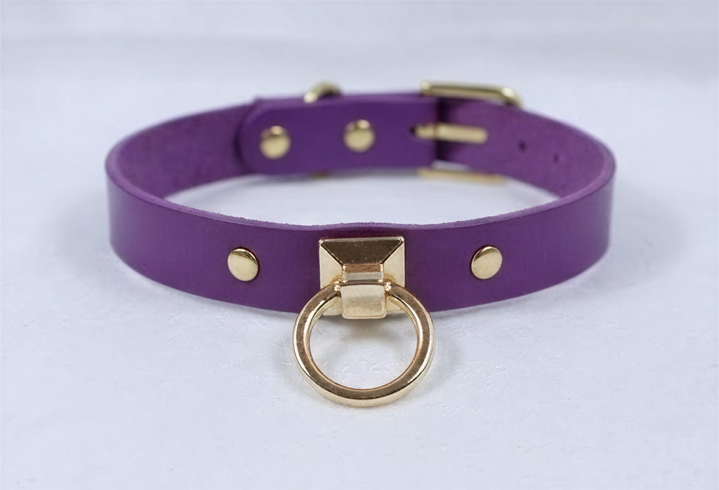A purple leather choker collar with a gold metal ring and three gold-colored studs on the front.