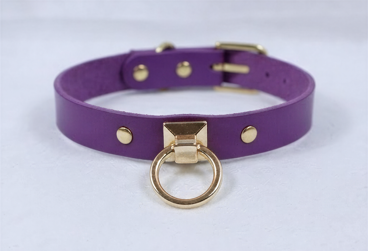 A purple leather choker collar with a gold metal ring and three gold-colored studs on the front.