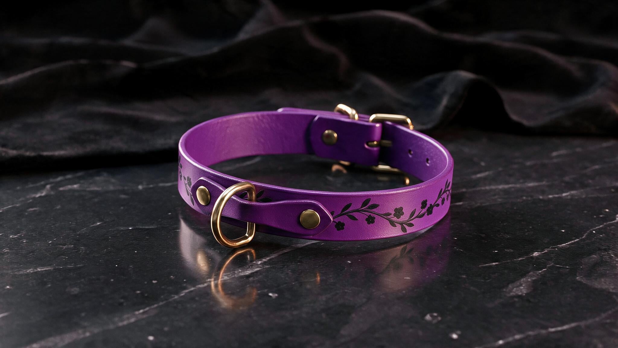A purple leather collar with a floral design sits on a dark surface.