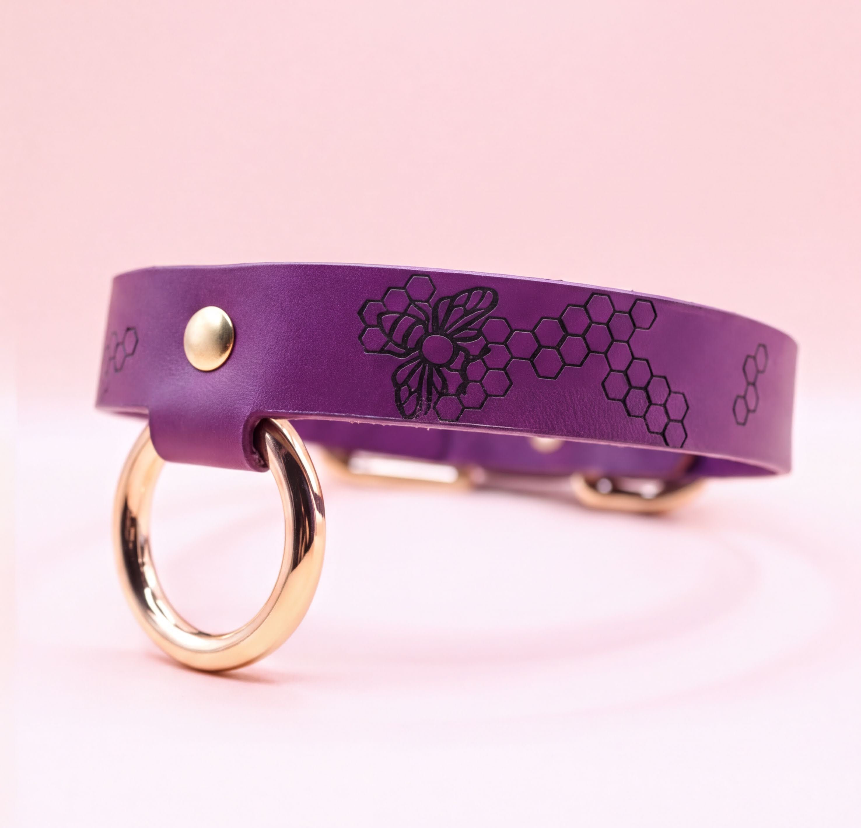A purple leather collar with a gold-colored metal ring and a floral pattern on the strap.
