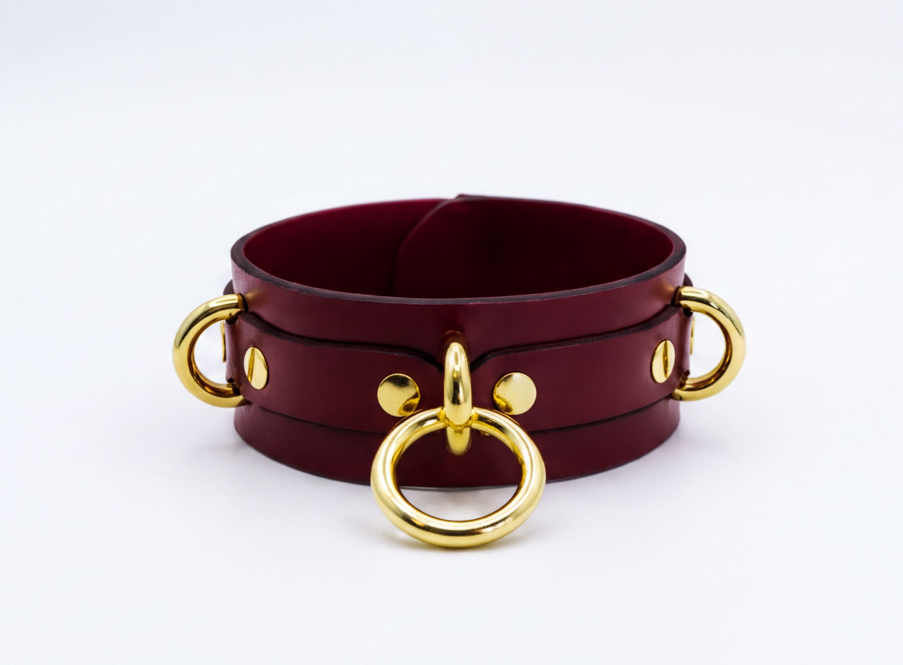 A burgundy leather choker necklace with gold-colored metal rings and buckles.