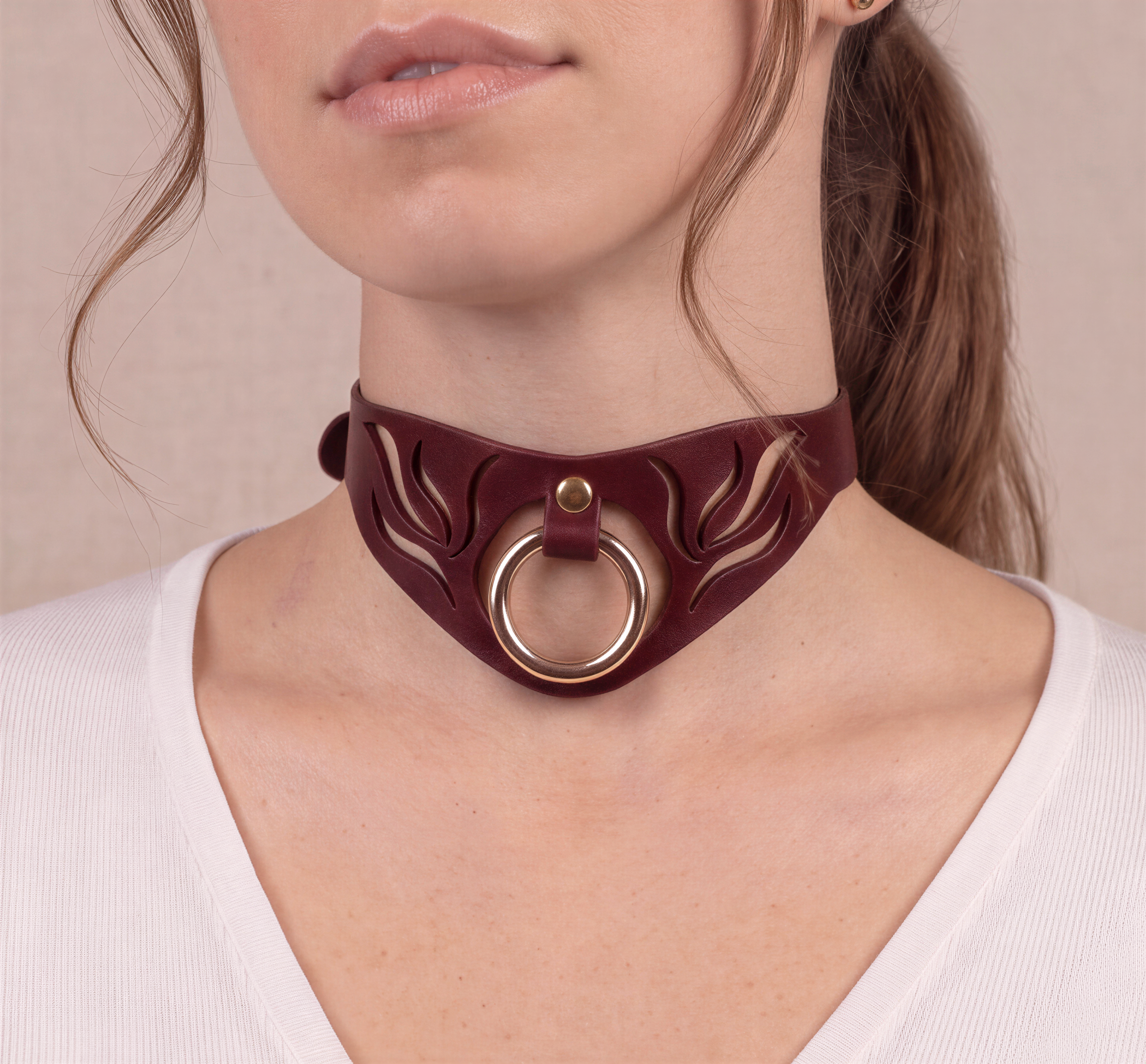 A close-up of a woman's neck and chest area wearing a burgundy choker necklace with a circular metal ring.