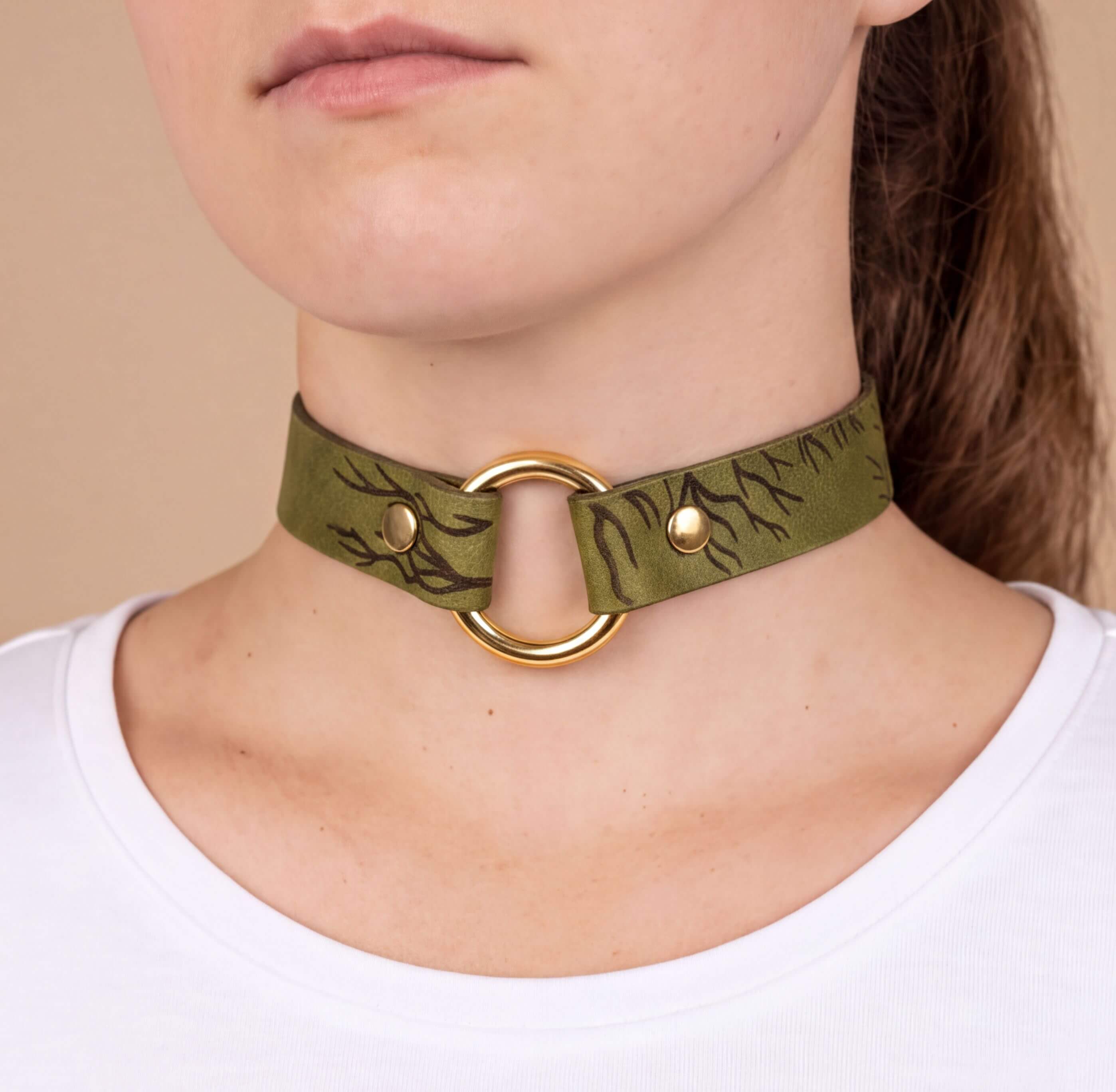 A close-up of a woman's neck wearing a green choker necklace with a gold ring.