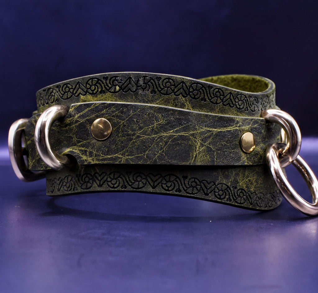 A green leather strap with metal rings and a decorative pattern on it, resting on a dark blue surface.