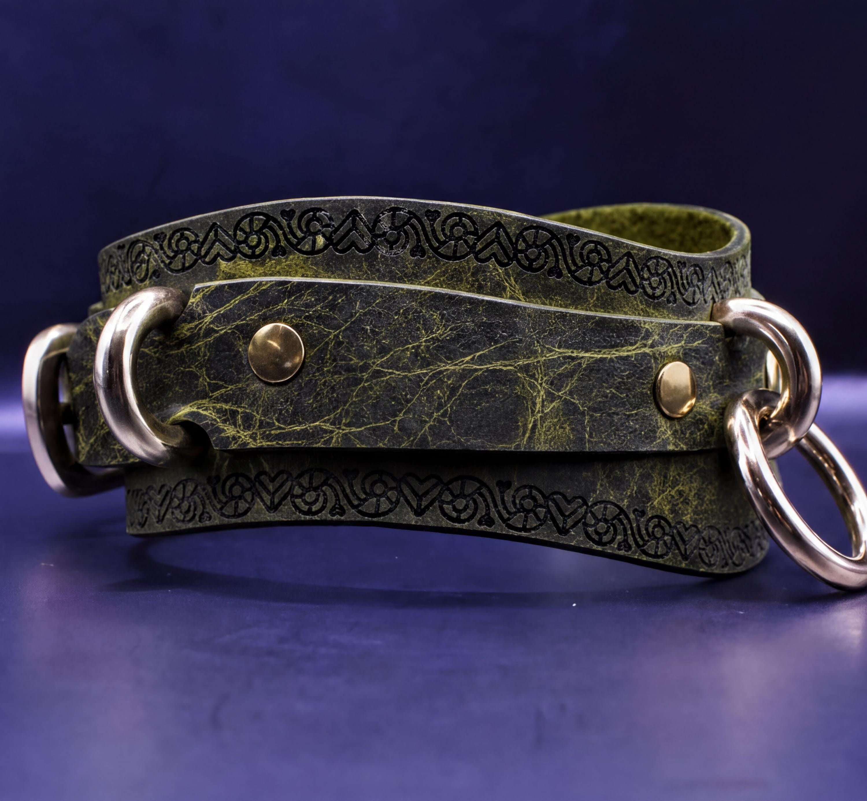 A green leather strap with metal rings and a decorative pattern on it, resting on a dark blue surface.