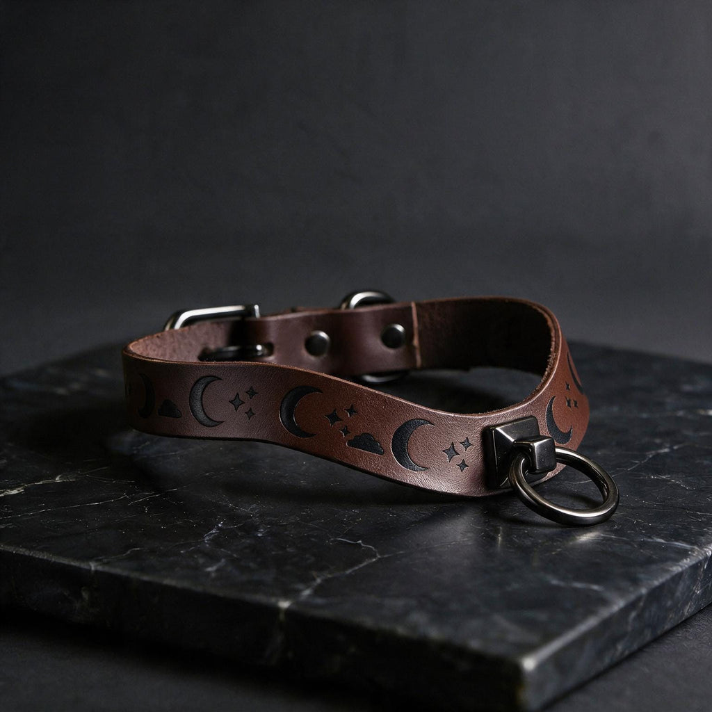 A leather collar with moon and star designs on it, resting on a dark surface.