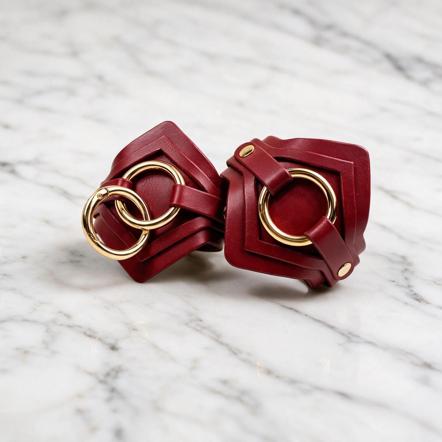 a pair of red leather straps with gold rings, placed on a marble surface.