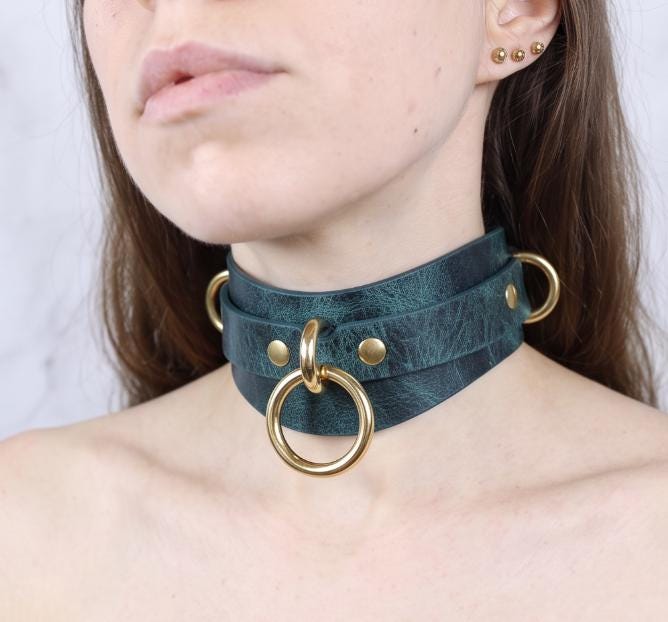 A close-up of a woman's neck and chest area wearing a dark green choker necklace with gold-colored metal rings.