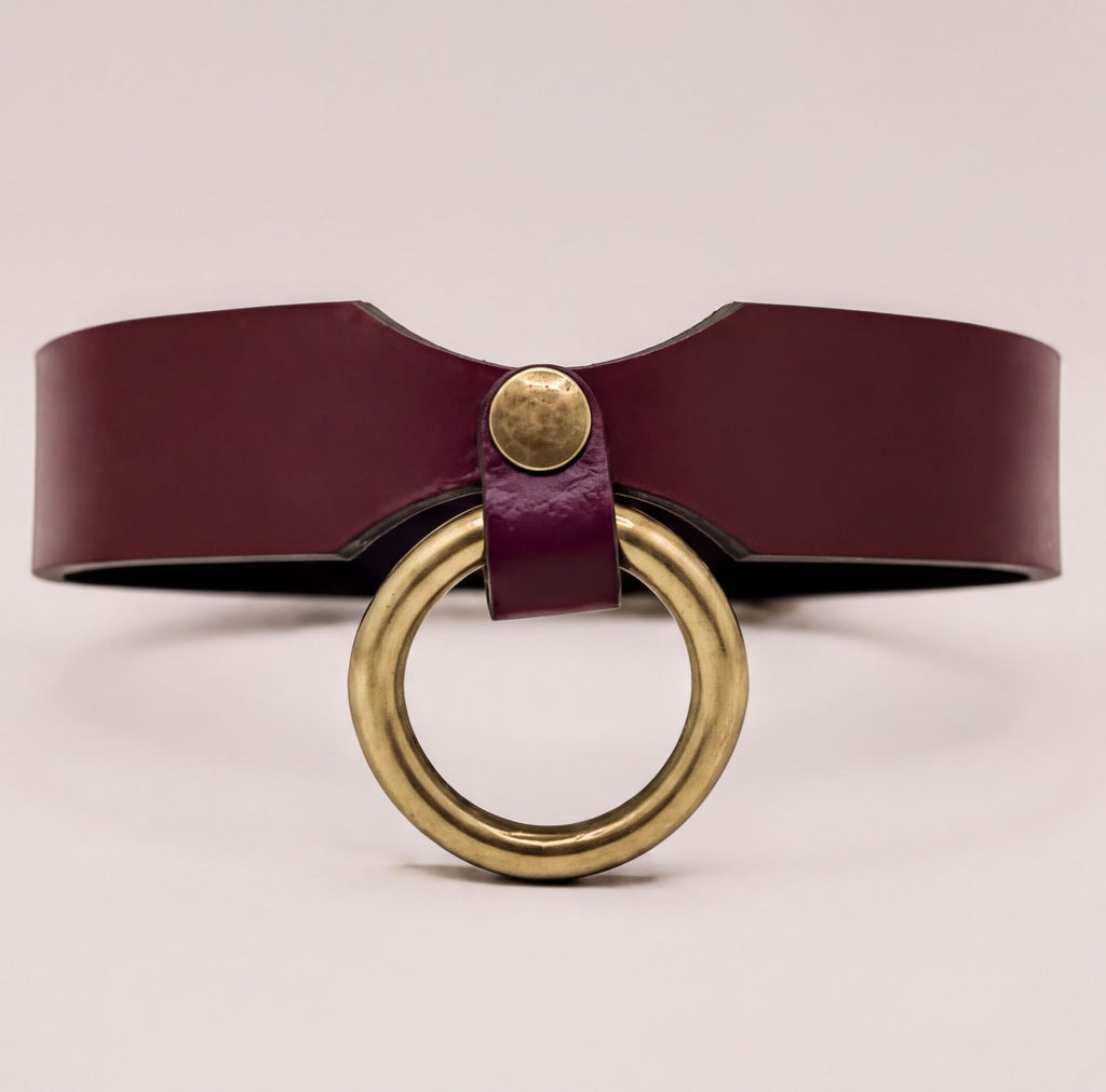 A burgundy leather choker necklace with a brass ring accent.