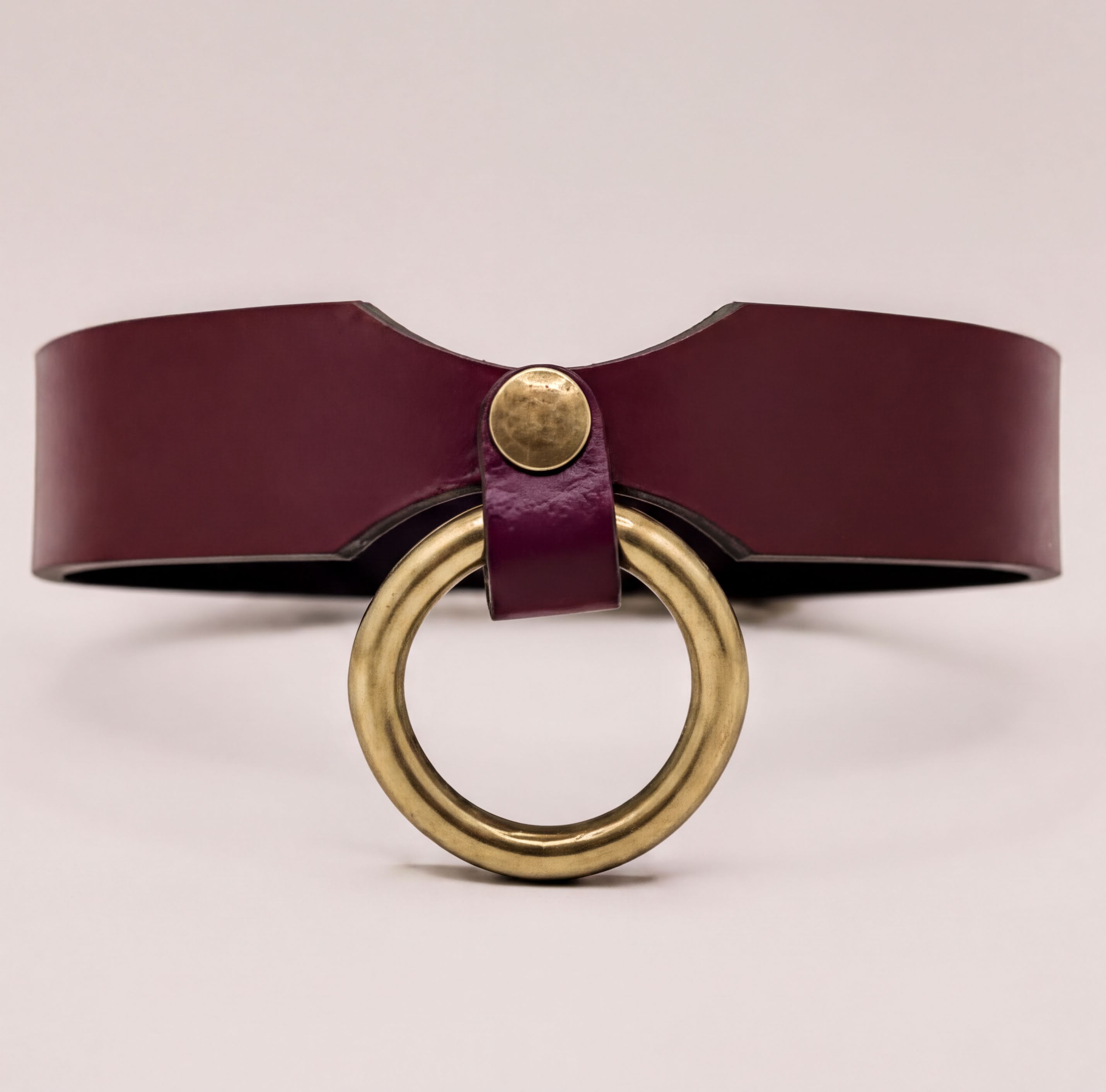 A burgundy leather choker necklace with a brass ring accent.
