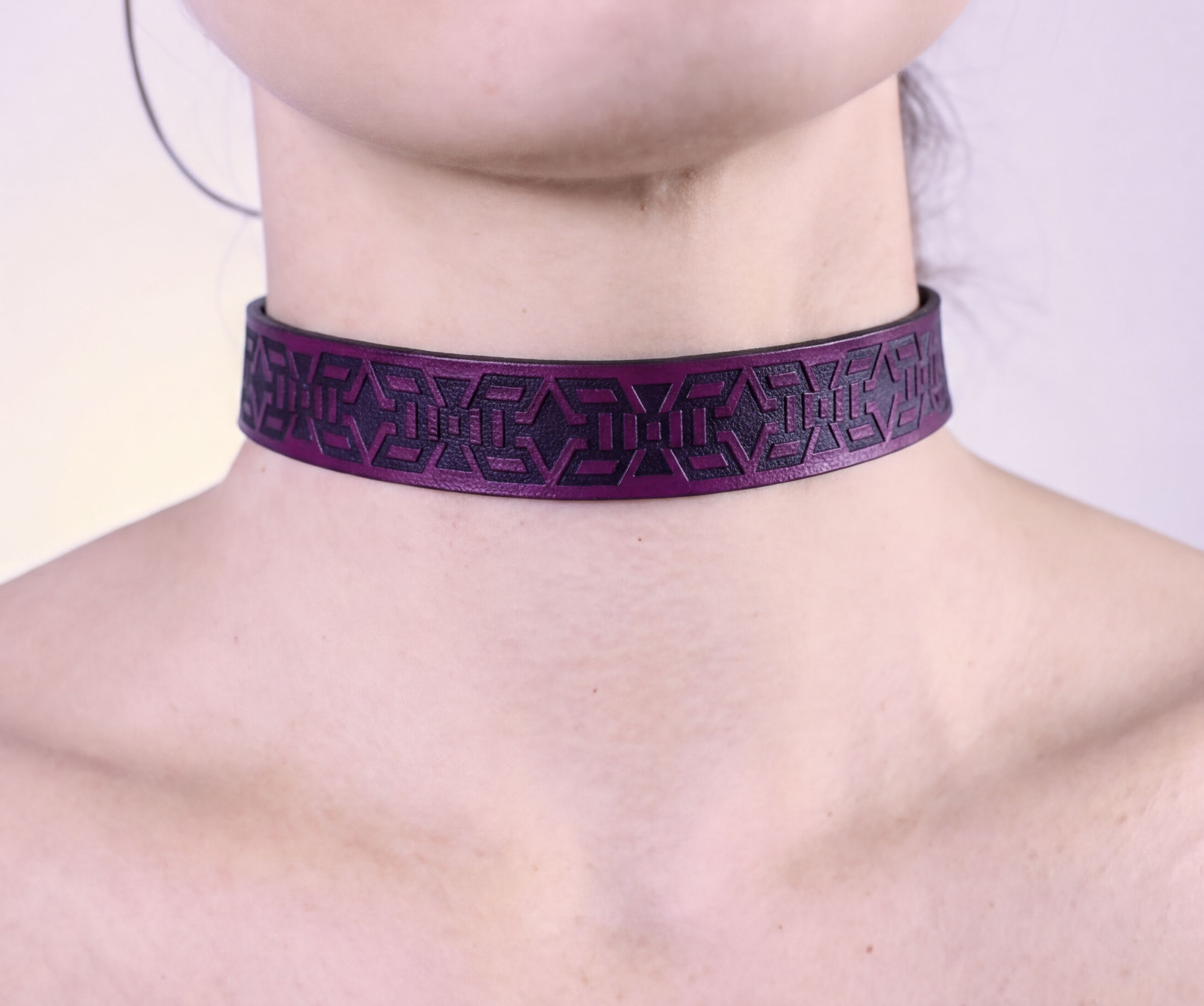 A close-up view of a person's neck and chest area wearing a purple choker necklace with a geometric pattern.