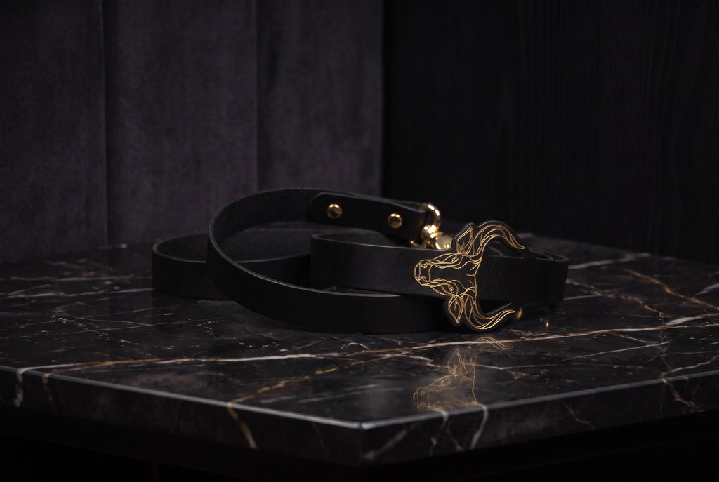A black leather belt with a gold buckle is placed on a black marble surface.