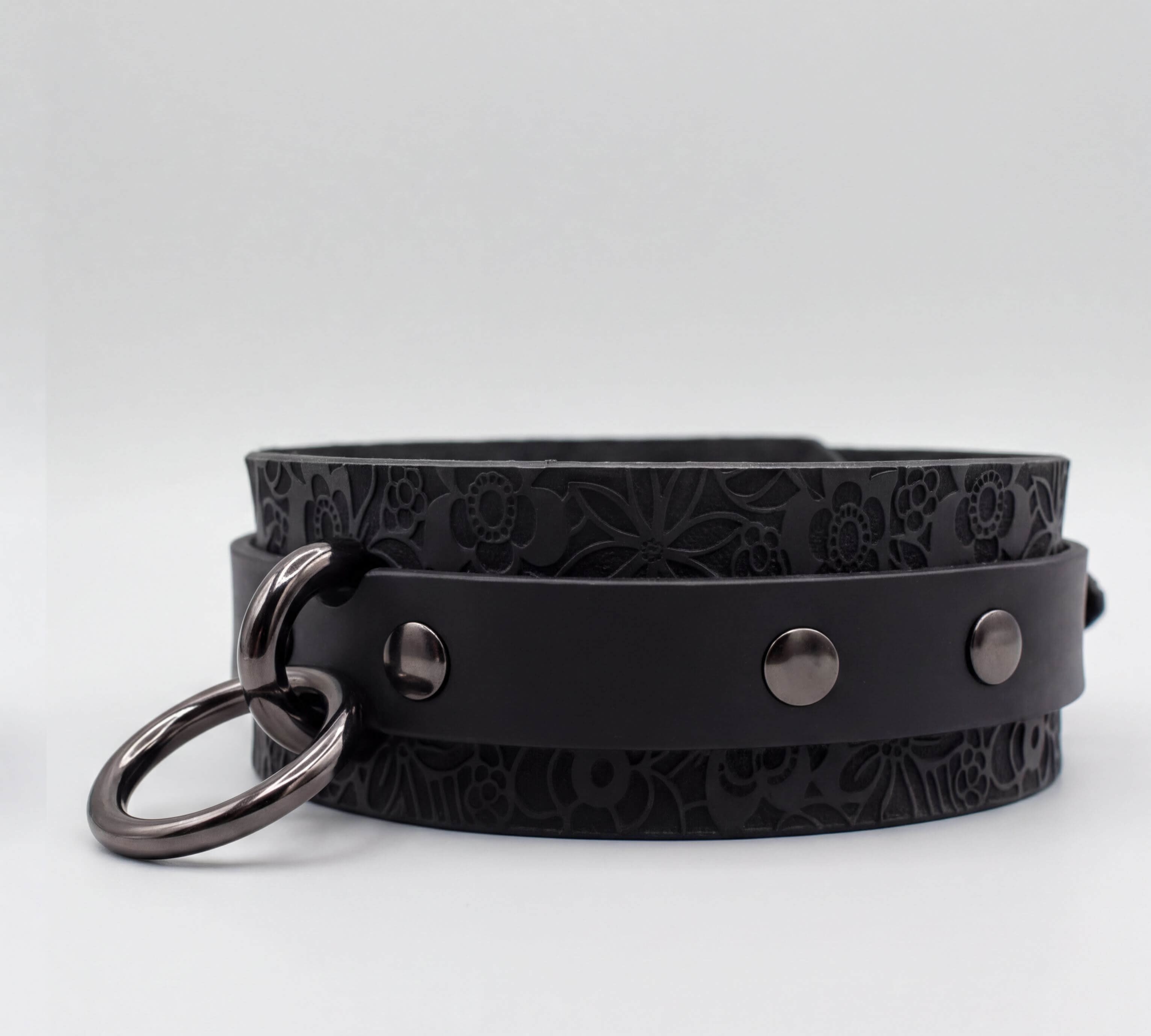 A black leather choker collar with metal rings and three circular buttons.