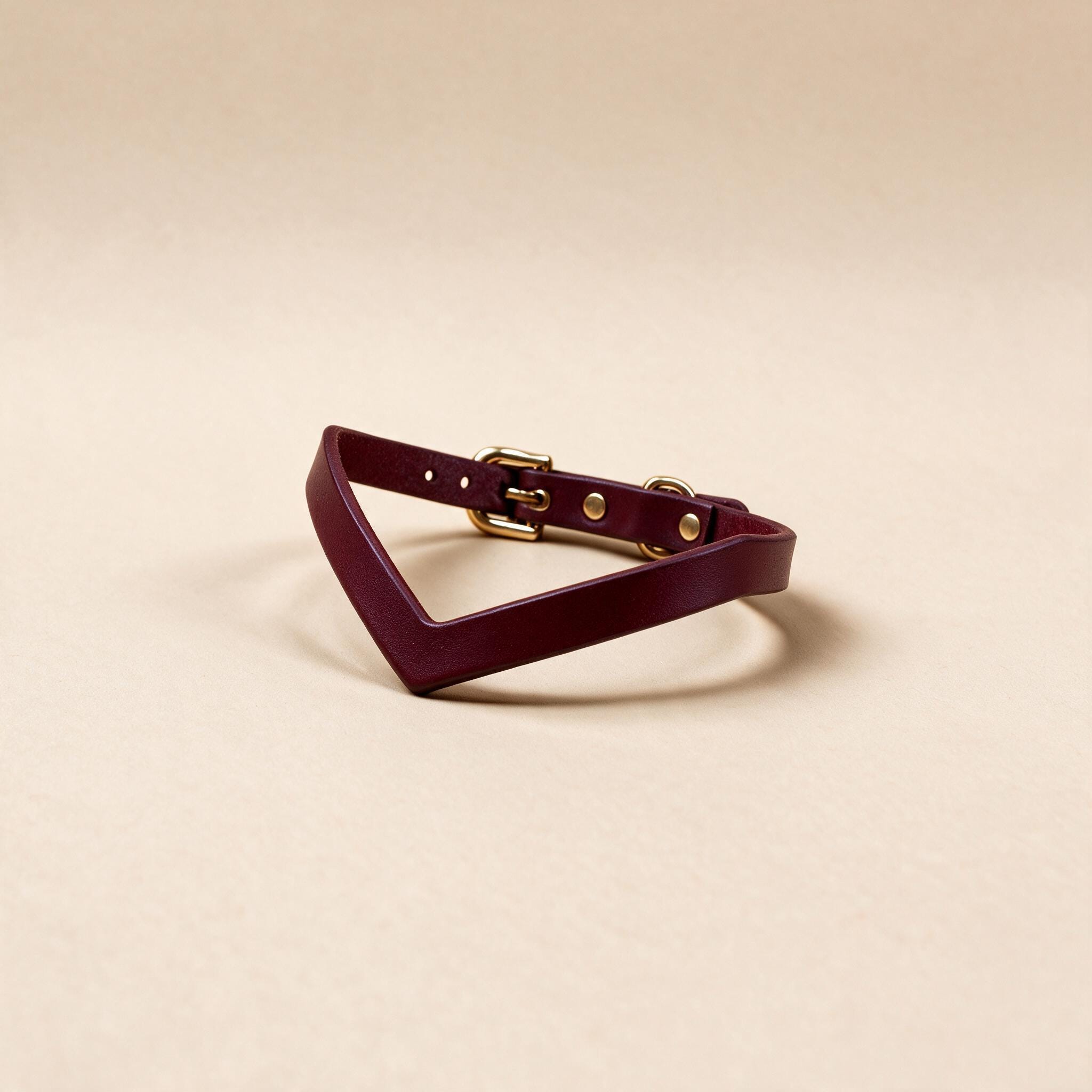 A burgundy leather choker necklace with a gold buckle is displayed against a beige background.