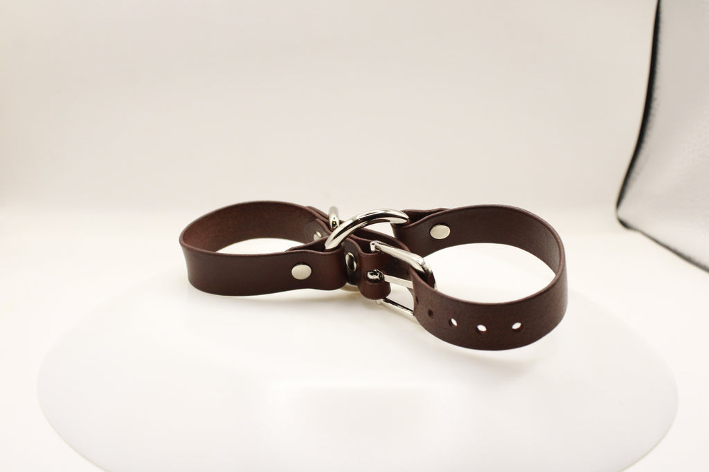 A brown leather strap with metal buckles and holes is shown against a white background.
