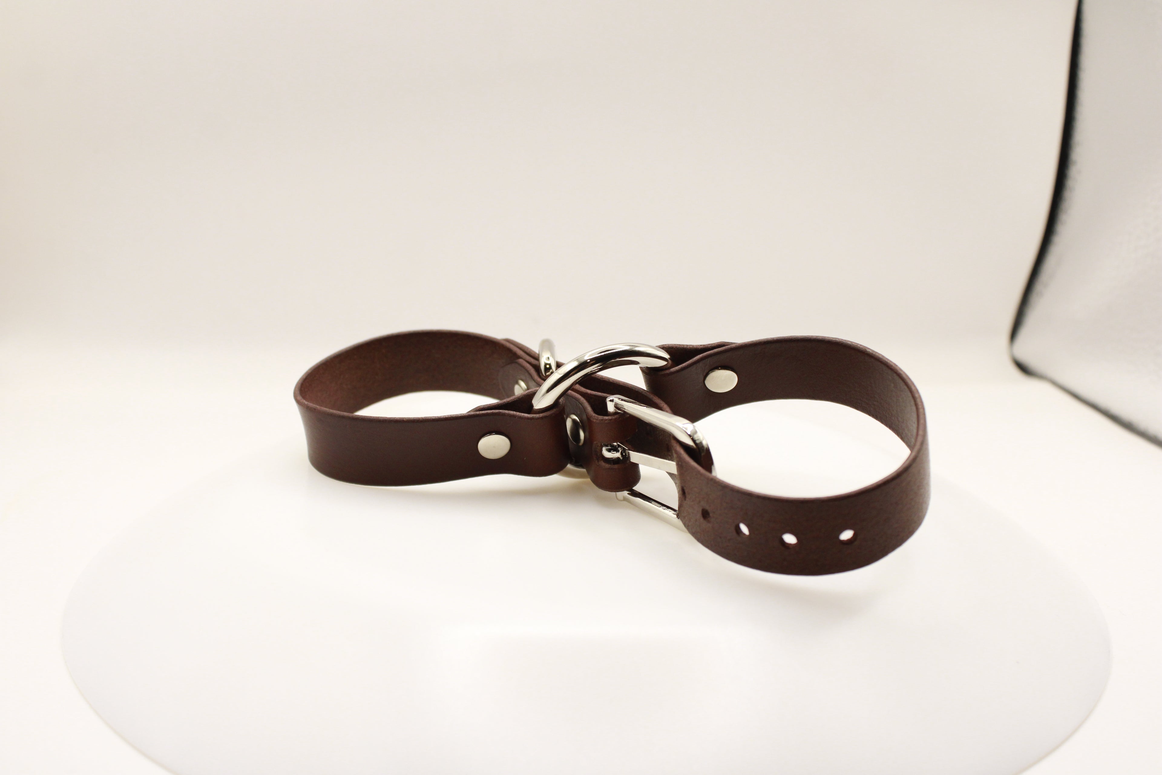 A brown leather strap with metal buckles and holes is shown against a white background.