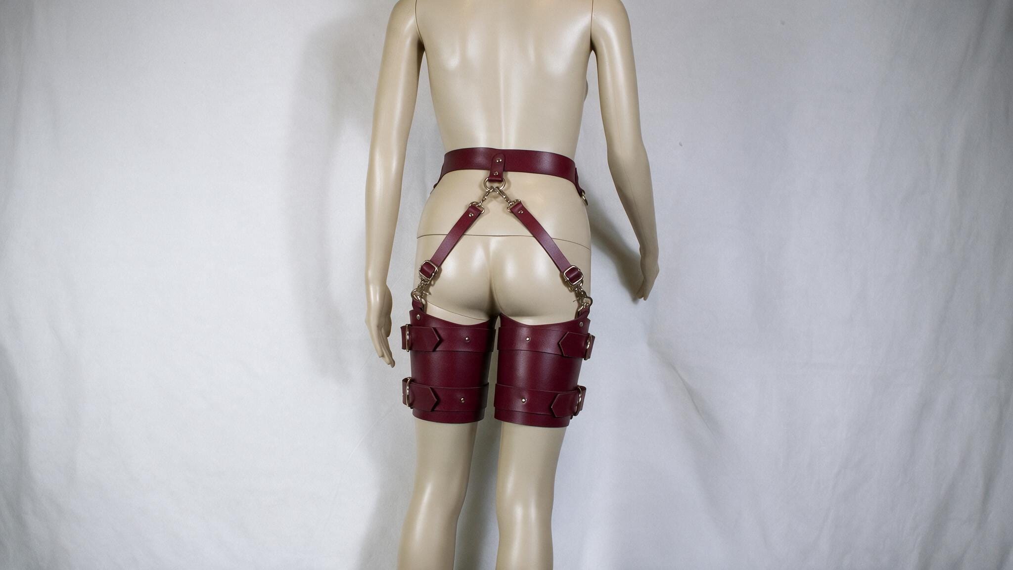 A mannequin wearing a pair of burgundy leather garter belts and garter belt straps.