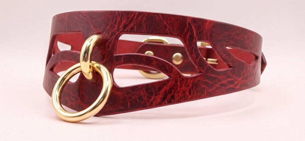 A close-up image of a burgundy leather choker necklace with a gold-colored ring and a cutout design on the front.
