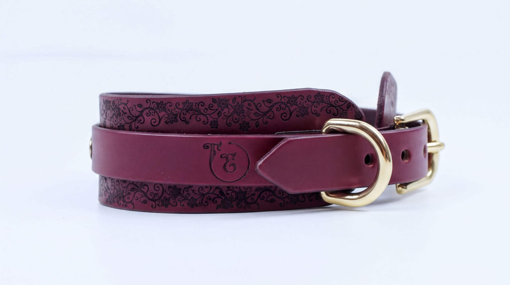 A burgundy leather belt with a gold buckle, featuring a decorative pattern on the surface.
