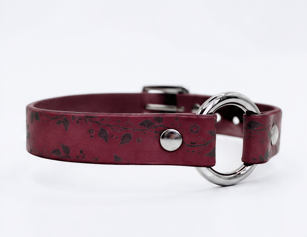 A burgundy leather collar with a silver metal ring and a leaf pattern design.