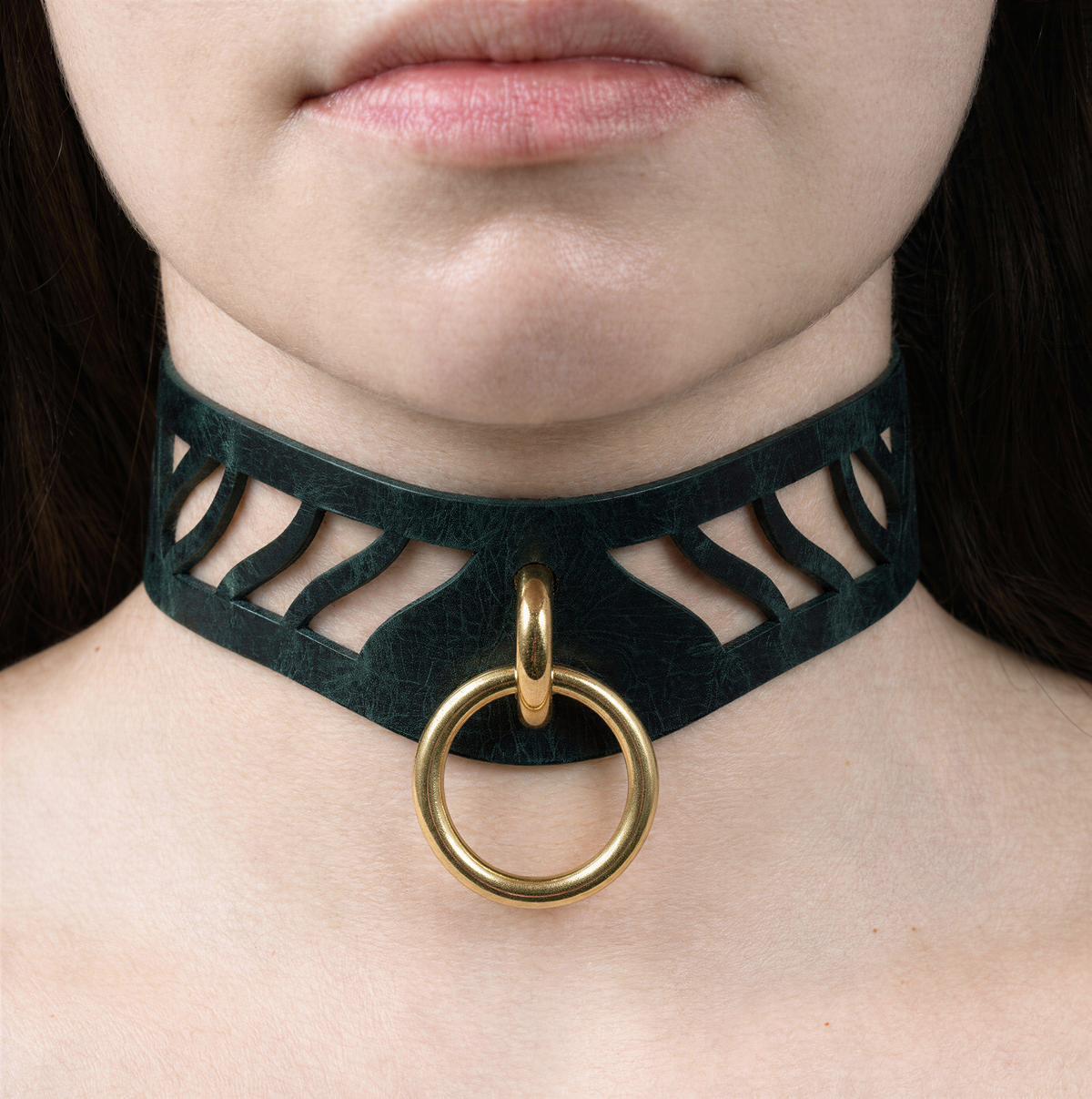 A close-up of a woman's neck and chin area, featuring a black choker necklace with a gold ring and a cutout design.