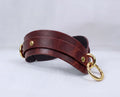 A brown leather strap with gold-colored metal rings and buckles, displayed on a white background.