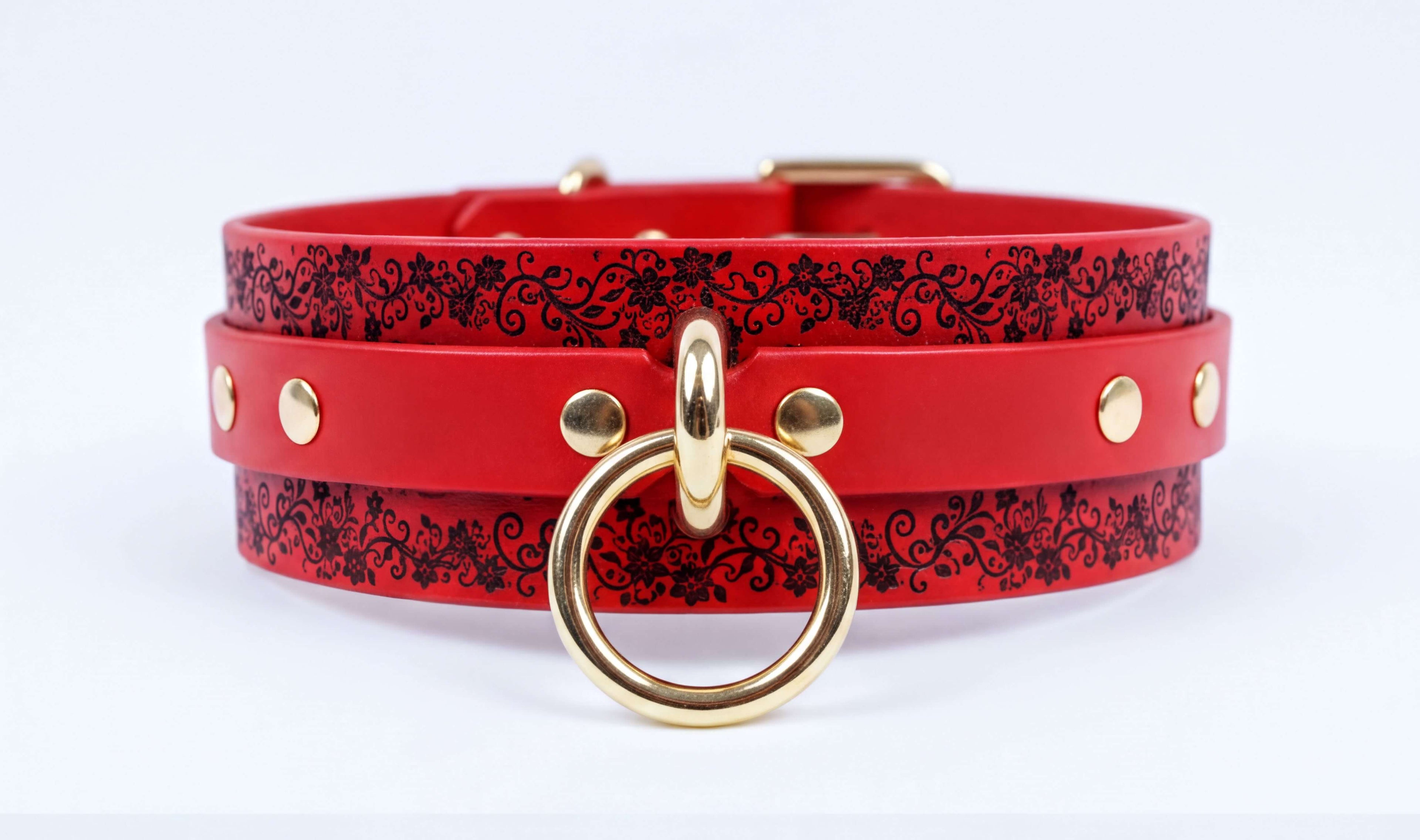 A red leather choker necklace with a gold-colored metal ring and decorative floral patterns on the straps.