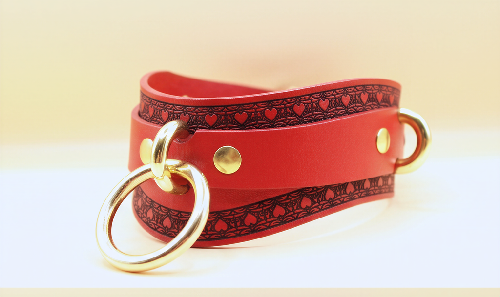 A red leather choker necklace with a gold ring and decorative pattern on the straps.