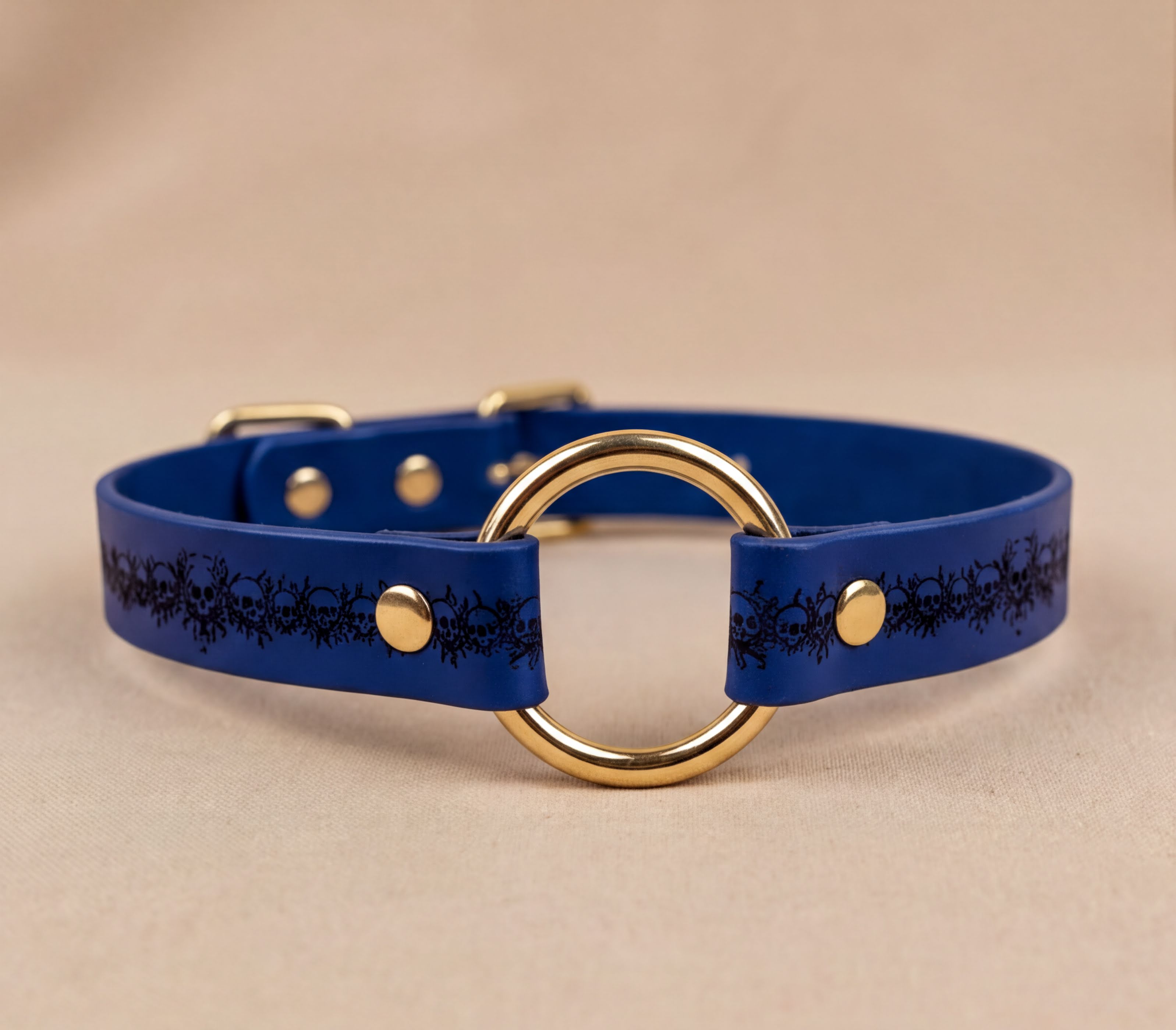 A blue leather collar with a gold ring and decorative pattern on the side.