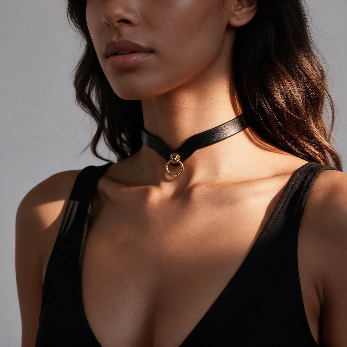 A close-up of a woman wearing a black choker necklace with a gold-colored pendant.