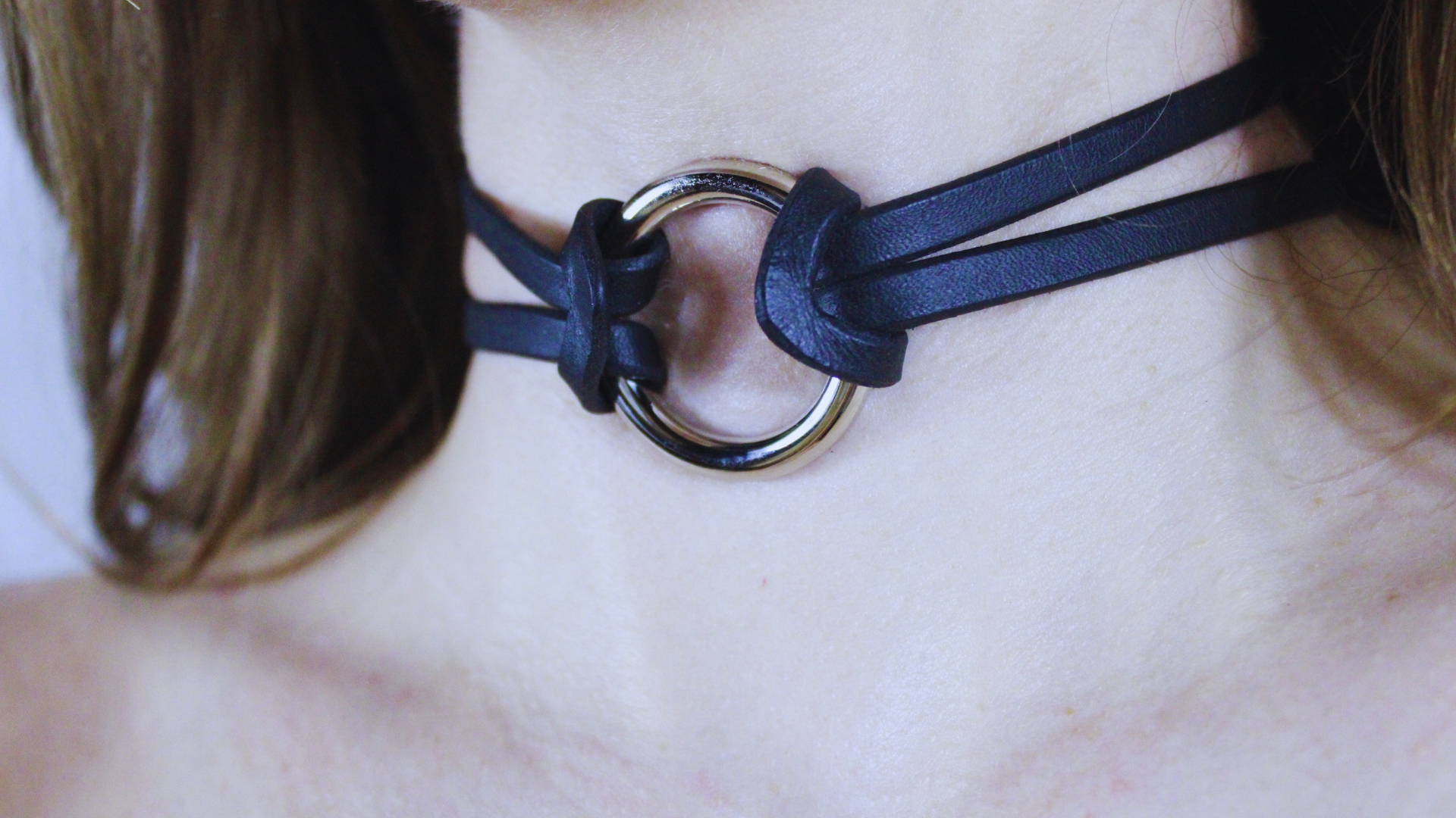 A close-up view of a person's neck and chin area, featuring a black leather choker necklace with a metal ring.