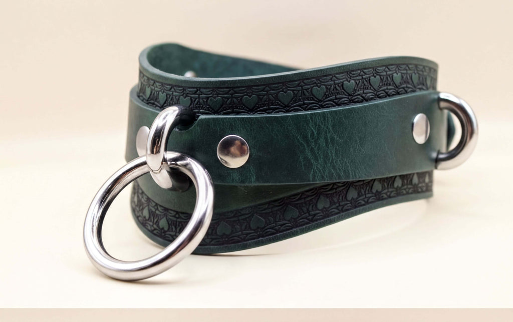 A close-up view of a green leather choker necklace with metal rings and a decorative pattern on the clasp.