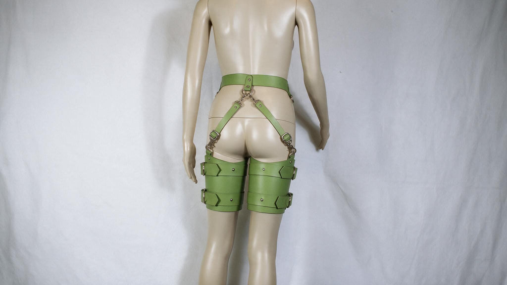 A mannequin wearing green leather straps and garter belts against a white background.