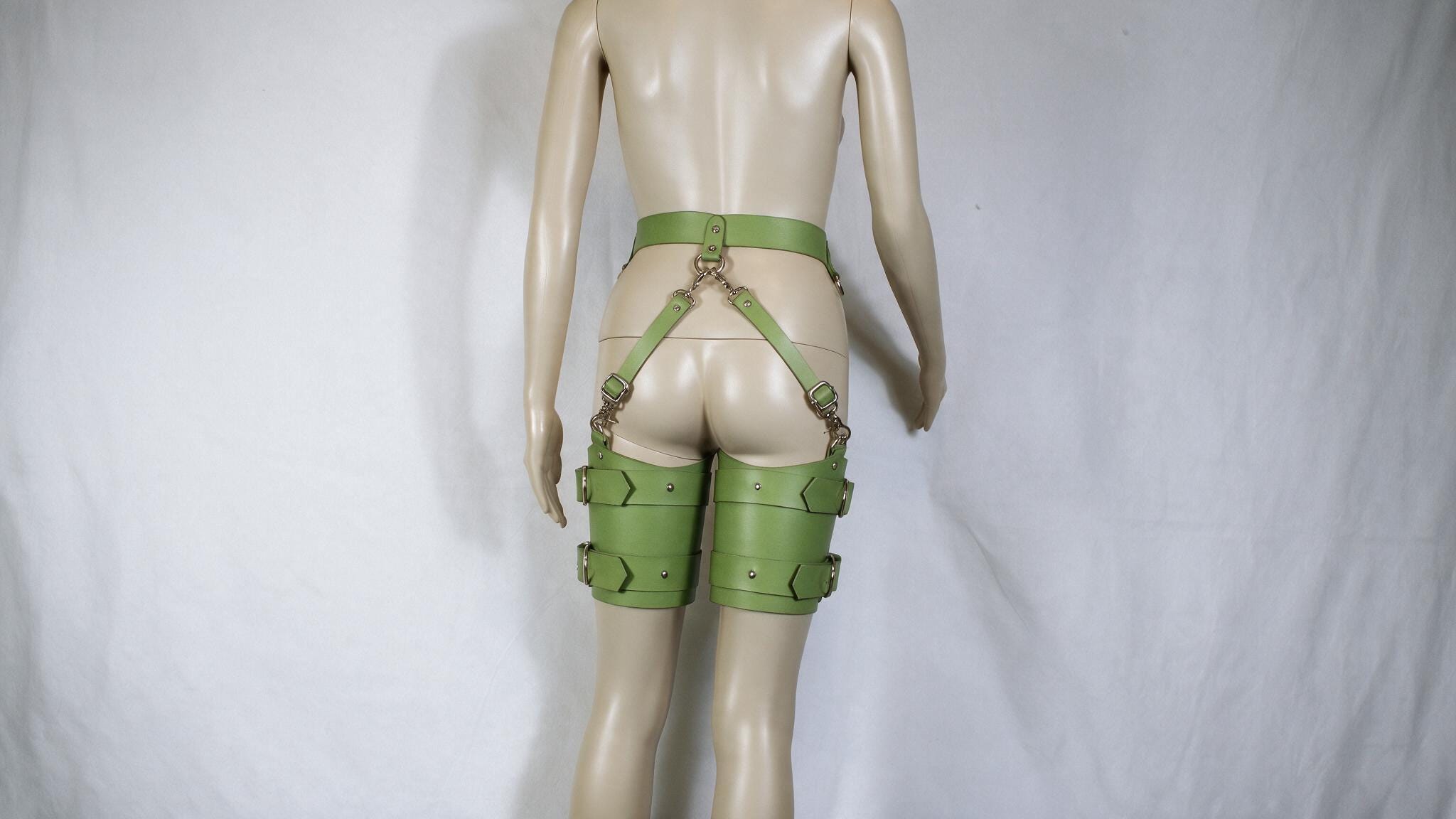 A mannequin wearing green leather straps and garter belts against a white background.