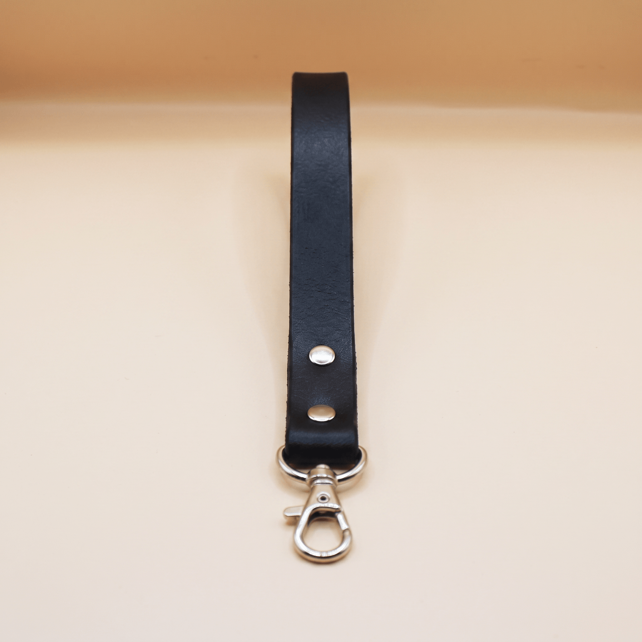 A black leather strap with a metal clasp and hook attached to it.