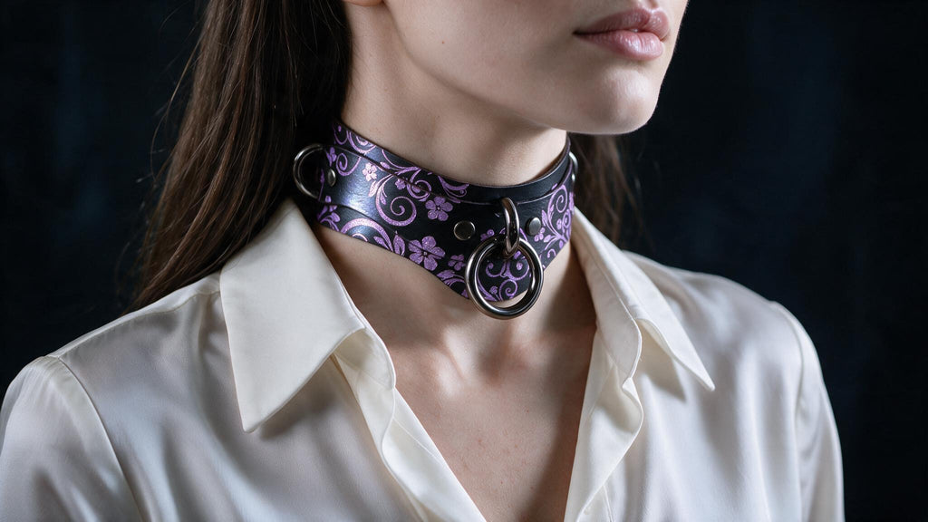 A close-up of a woman wearing a choker necklace with a floral pattern and a metal ring.
